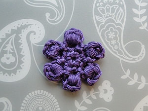 A small purple flower using a bullion stitch for each petal